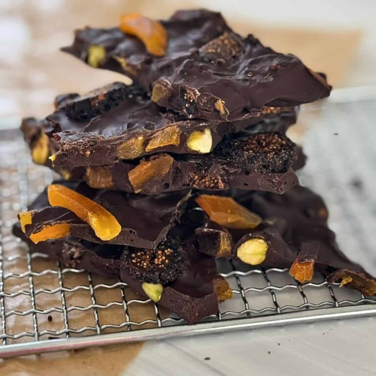 dark chocolate bark with orange, fig, and pistachios stacked on a wire rack. 