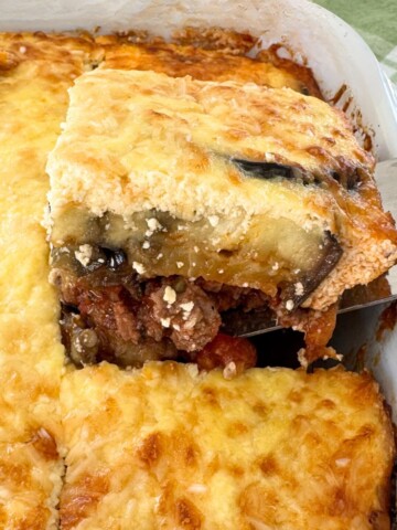 Lamb moussaka being lifted with a spatula out of the casserole to show the layers.