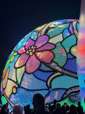 The sphere all lit up at night in bright colors and flowers.