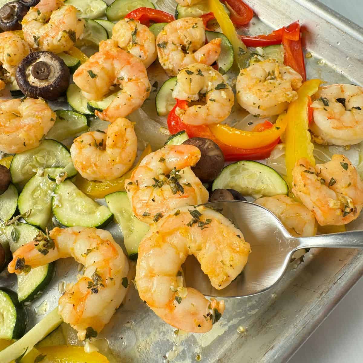 Using a spoon to lift off a shrimp from the sheet pan. 