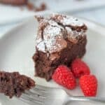 A slice of flourless chocolate cake on a white plate with a fork holding one piece.