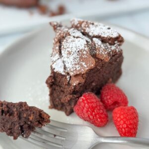 A slice of flourless chocolate cake on a white plate with a fork holding one piece.