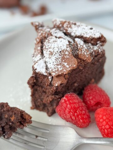 A slice of flourless chocolate cake on a white plate with a fork holding one piece.