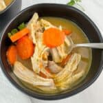 Grandma's chicken soup in a black bowl with a spoon lifting some out.