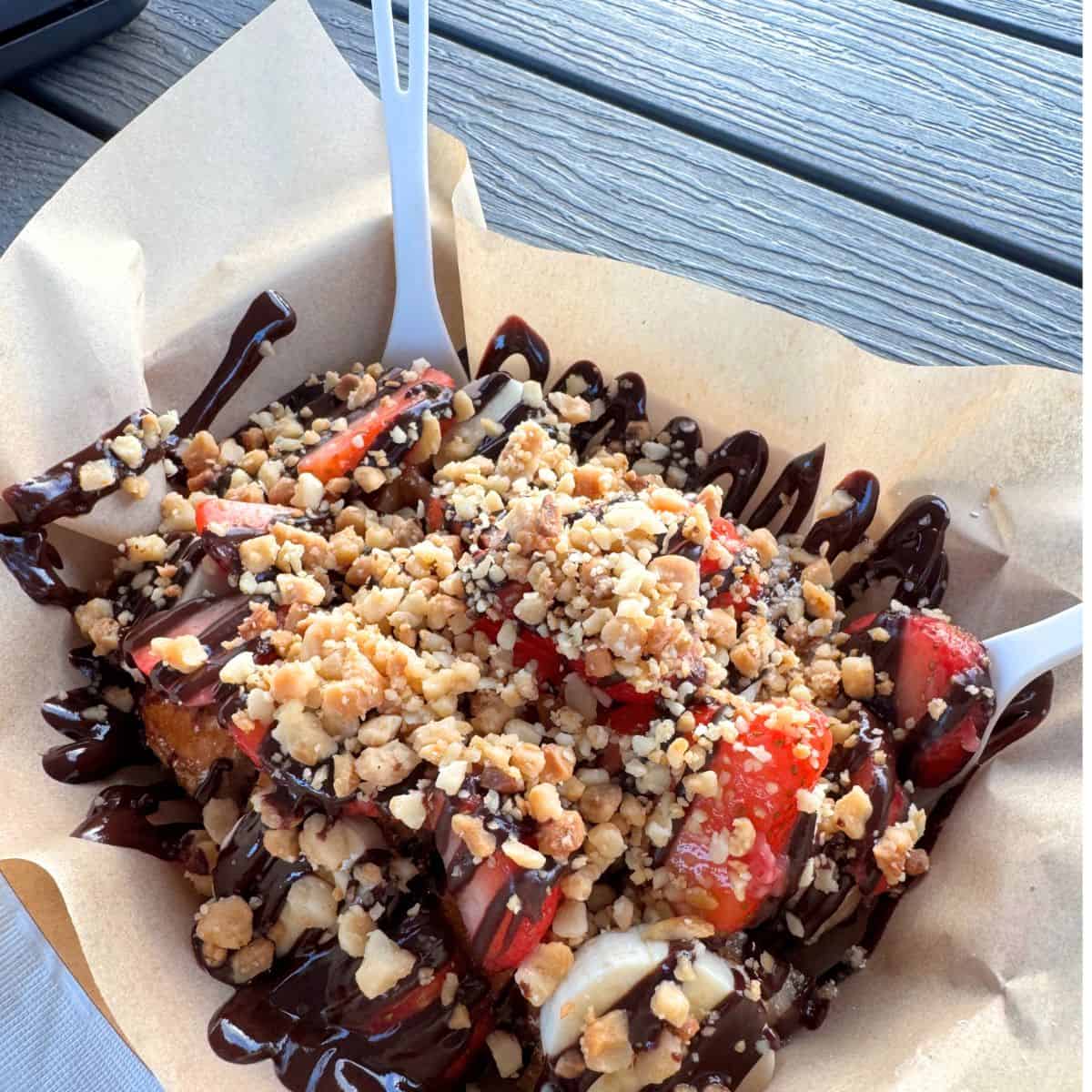 A waffle topped with bananas strawberries and macadamia nuts with a chocolate drizzle. 