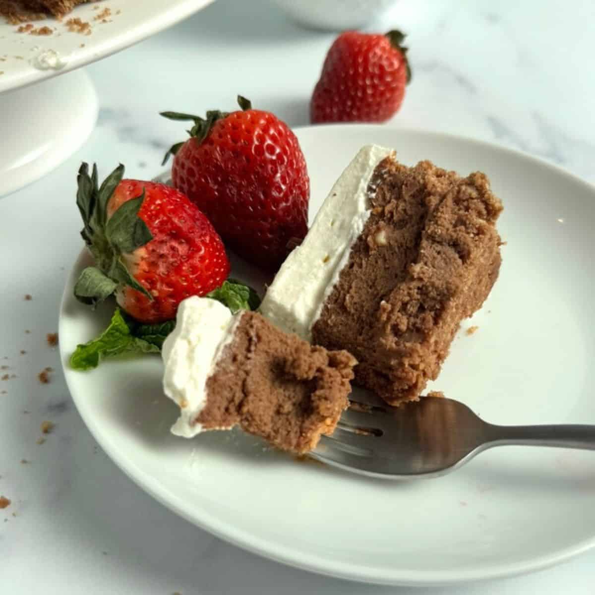 A fork holding a piece of the cheesecake while resting on a plate.