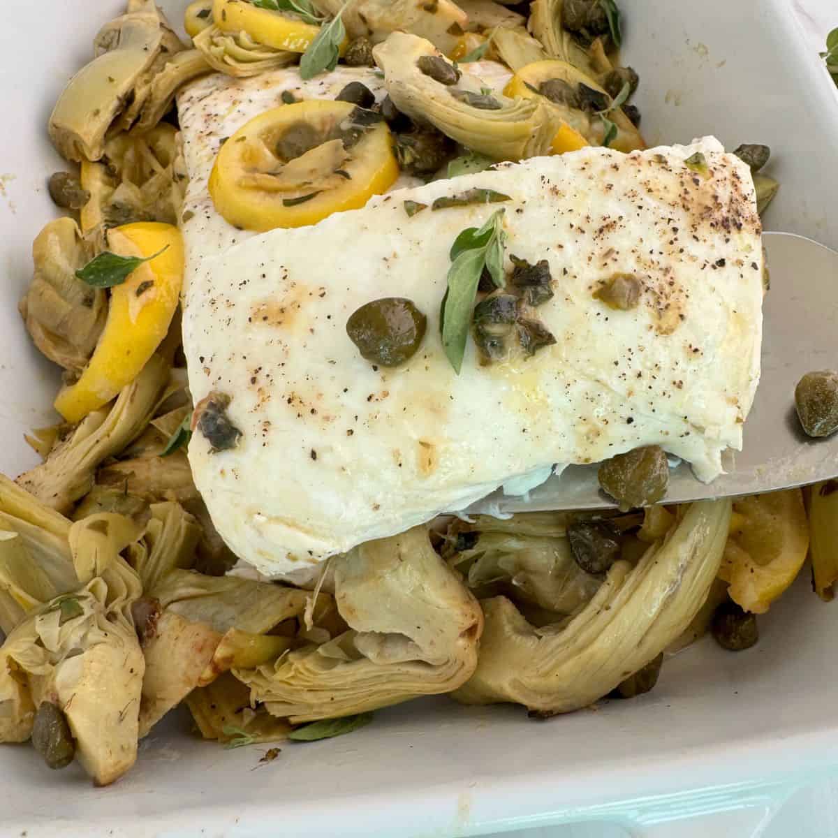 A slice of halibut lifted out of the casserole dish. 