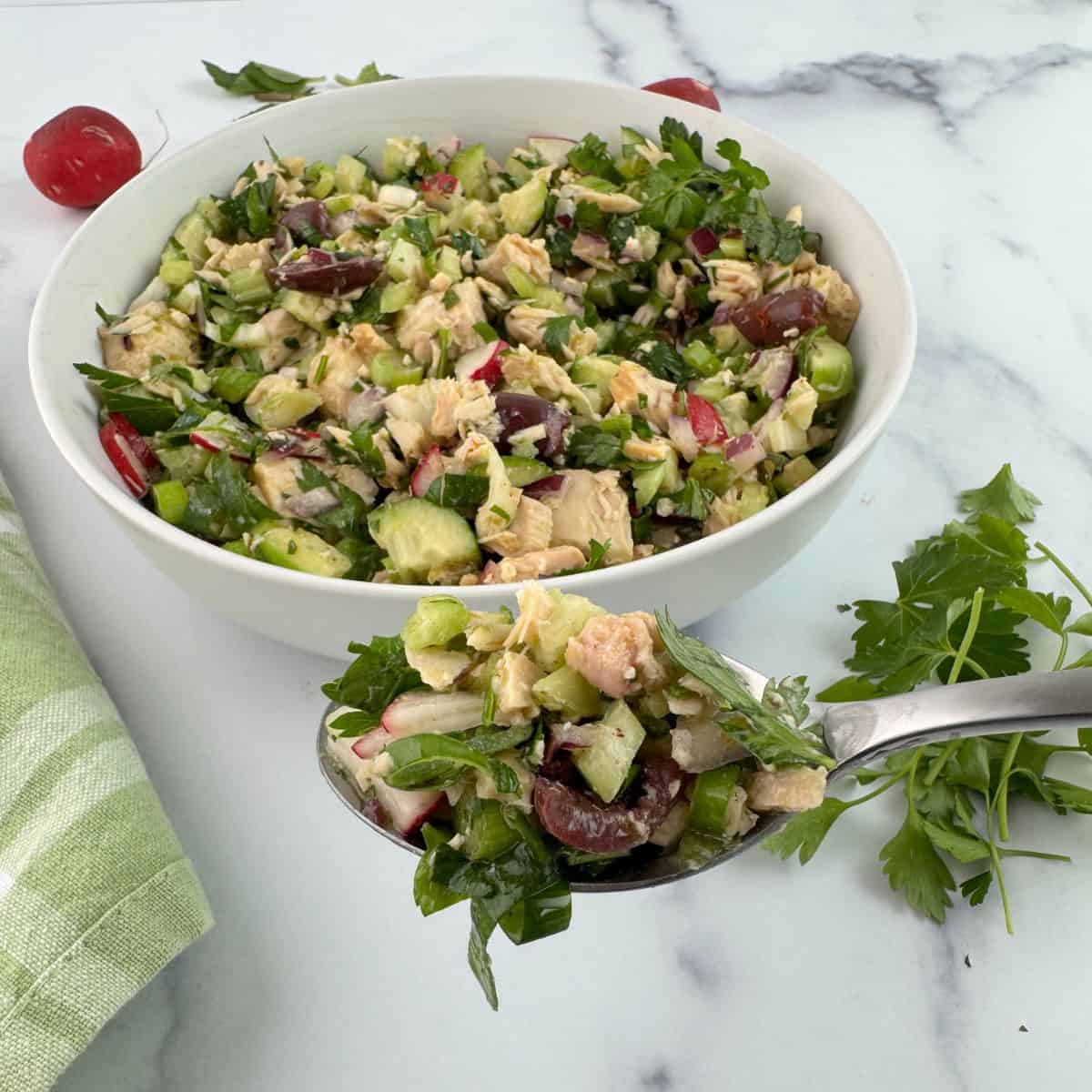 The bowl of Mediterranean tuna salad with a spoon lifting out one portion. 