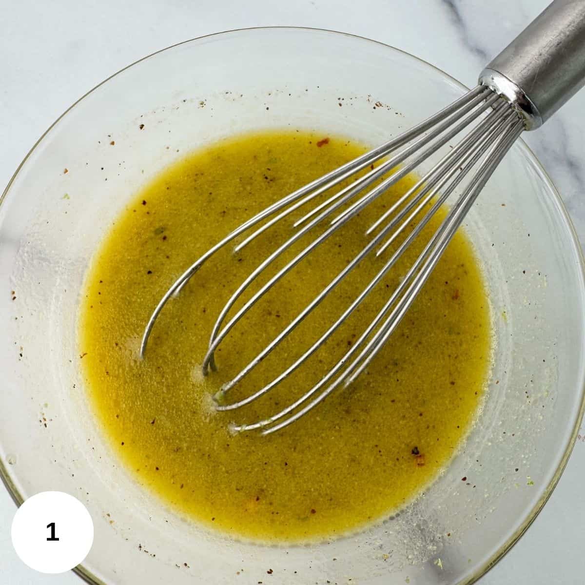 Whisking the dressing ingredients together in a clear bowl. 