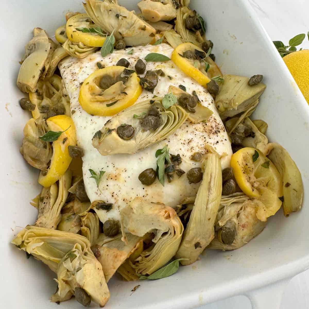 A picture of the halibut in the casserole dish with the sauce poured over the top. 