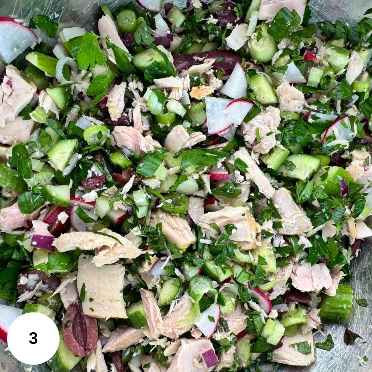 Adding the tuna to the salad ingredients and combining them. 