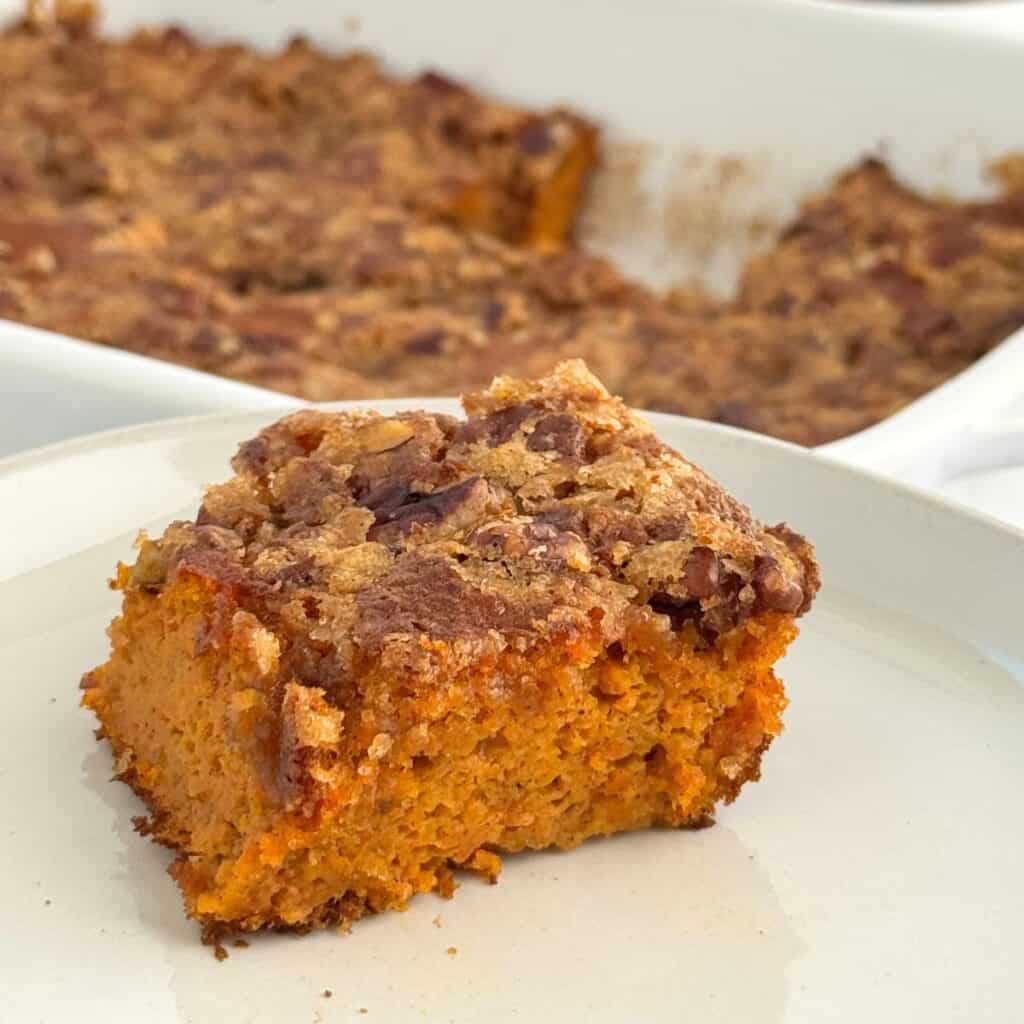 A piece of carrot kugel topped with pecans and brown sugar on a white plate.