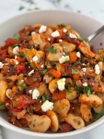 Greek baked beans, gigante plaki, in a white bowl with a spoon.