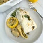 A slice of the halibut on a plate with the lemon caper artichoke sauce over the top.