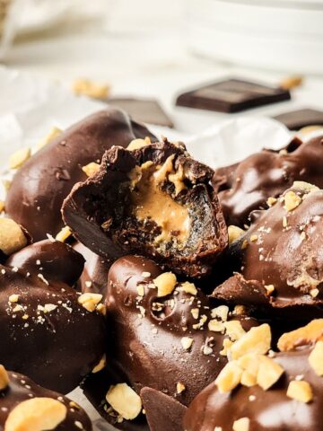 Chocolate covered stuffed dates stacked on top of each other and one is half eaten.