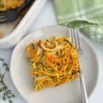 A slice of vegetable kugel on a white plate accompanied by a fork and green dish towel.