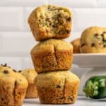 Gluten free zucchini muffins stacked on top of each other with the top muffin half eaten.