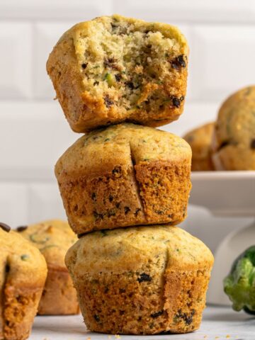 Gluten free zucchini muffins stacked on top of each other with the top muffin half eaten.