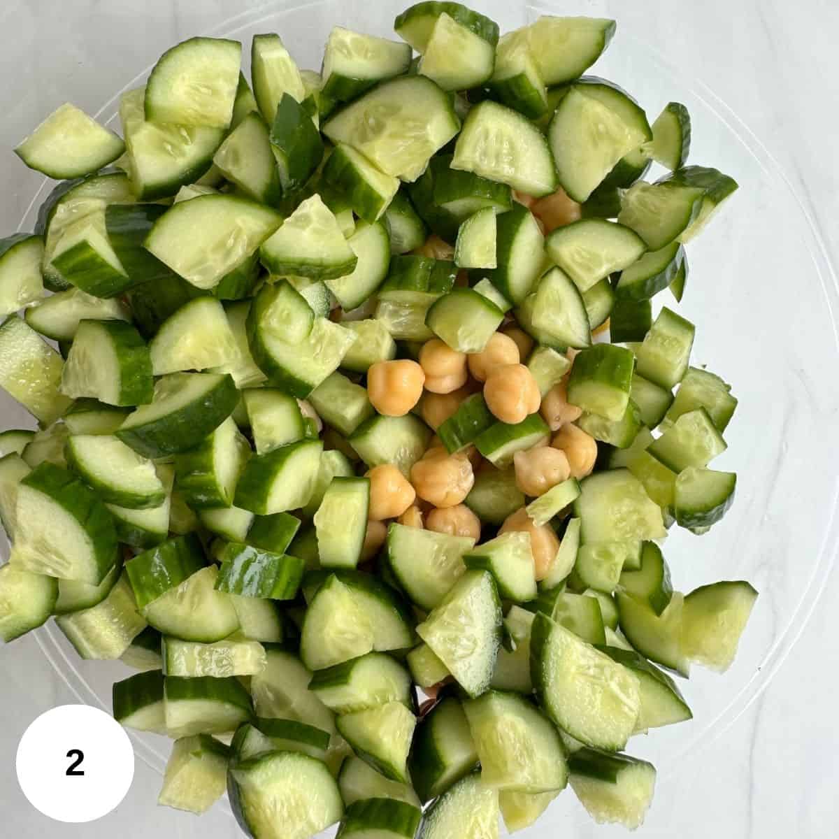Adding the cucumber, chickpeas, and tomatoes to a clear bowl.