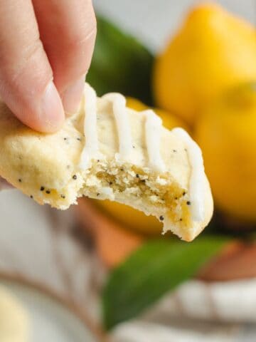 Someone holding a lemon poppy seed cookie after having taken a bite out of it.