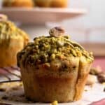 A pistachio muffin topped with pistachios and pistachio butter sitting on parchment paper.