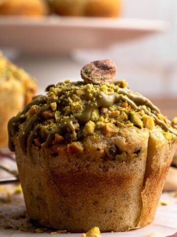 A pistachio muffin topped with pistachios and pistachio butter sitting on parchment paper.