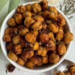 Roasted chickpeas with Mediterranean spices in a white bowl with a spoon and thyme.