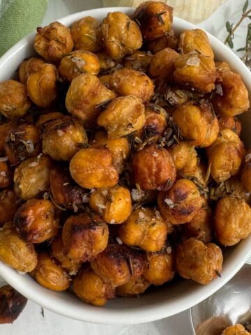 Roasted chickpeas with Mediterranean spices in a white bowl with a spoon and thyme.
