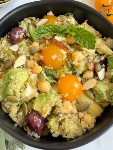 A bowl of zesty quinoa salad in a black bowl surrounded by tomatoes.