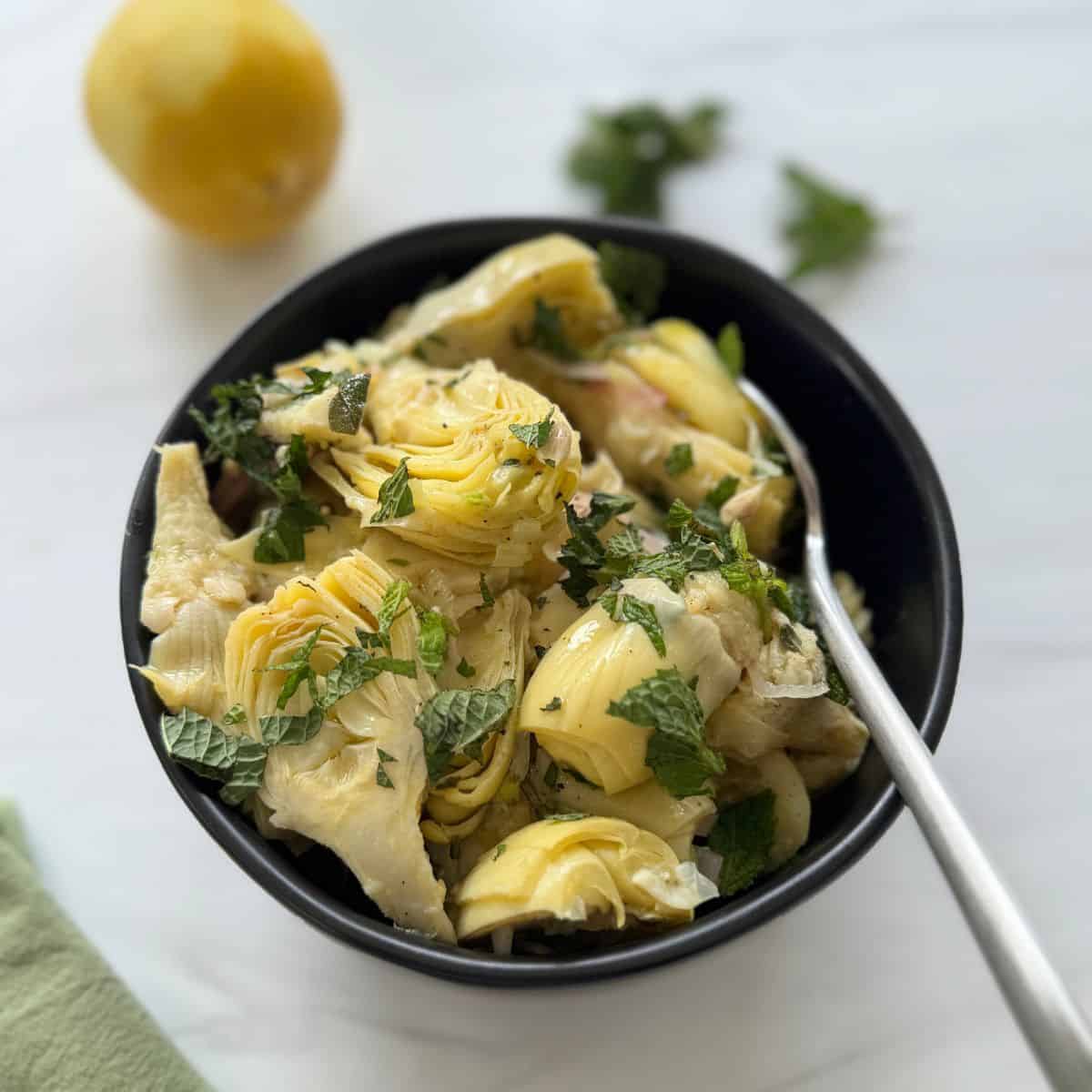 A black bowl filled with the marinated artichoke hearts and a spoon.