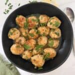 Chicken Piccata Meatballs in a black skillet with a spoon on the side.