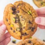 Someone breaking open the chocolate chip pistachio cookie to show the gooey interior.