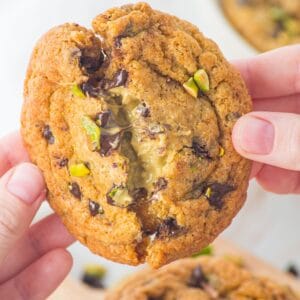 Someone breaking open the chocolate chip pistachio cookie to show the gooey interior.