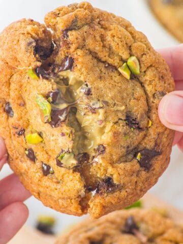 Someone breaking open the chocolate chip pistachio cookie to show the gooey interior.
