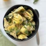 A bowl of marinated artichokes with chopped mint on top and a spoon.
