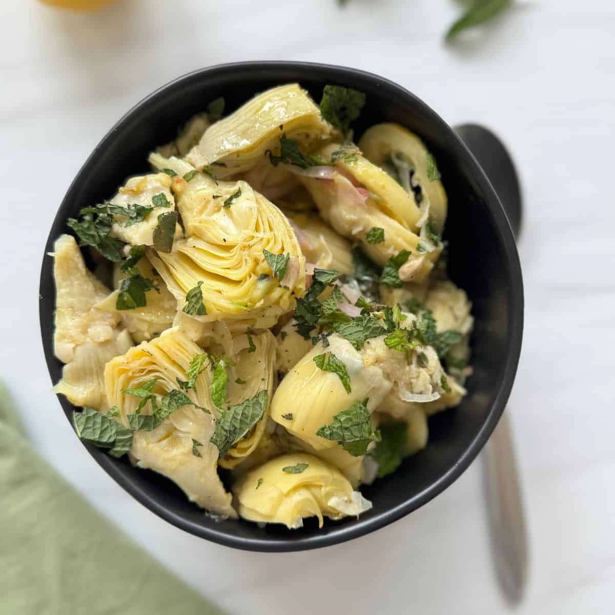 A bowl of marinated artichokes with chopped mint on top and a spoon.