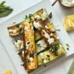 A plate with roasted zucchini halves topped with a lemon yogurt sauce and chopped mint.