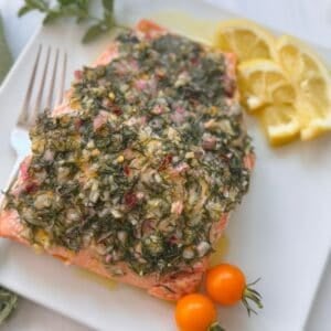 Mediterranean Salmon on a plate with a side of lemons and cherry tomatoes.