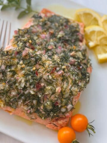 Mediterranean Salmon on a plate with a side of lemons and cherry tomatoes.