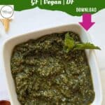 A white bowl filled with vibrant green mint pesto, garnished with a mint leaf. Text above reads “Mint Pesto GF | Vegan | DF” with a pink arrow pointing to “Download.” A white background and a partial wooden spoon are visible.