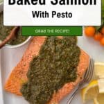 A baked salmon fillet topped with vibrant salmon pesto is served on a white plate with lemon wedges, a fork, cherry tomatoes, and a small bowl of pesto. Text overlay reads: Quick & Easy Baked Salmon With Pesto. Grab the recipe!.