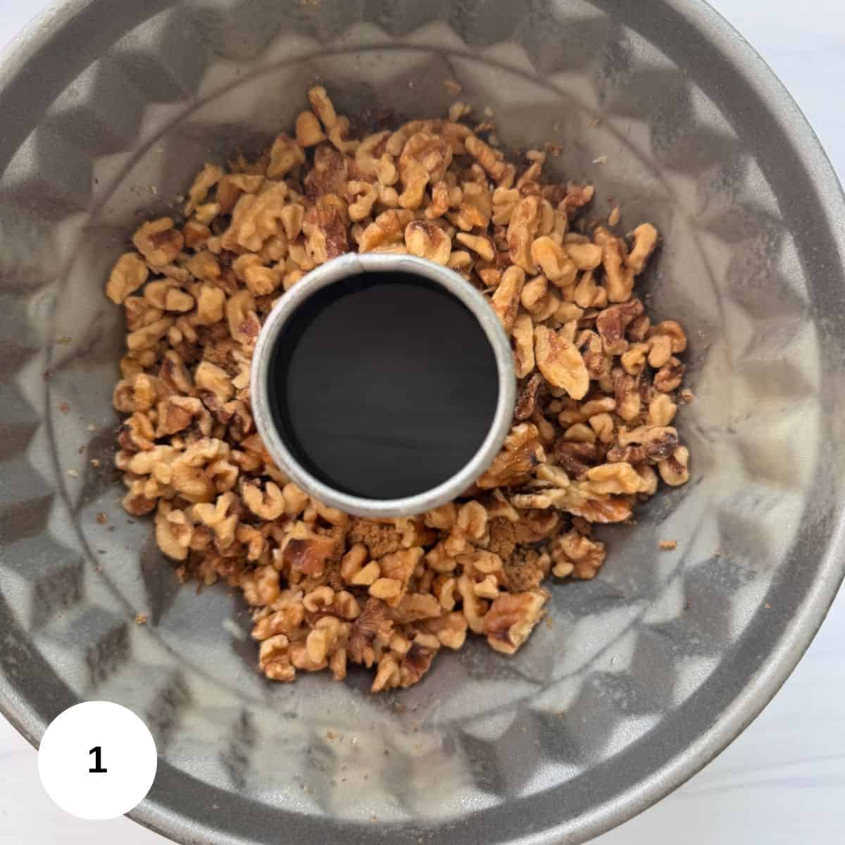 Chopped walnuts and raisins spread evenly at the bottom of a greased Bundt cake pan, shown from above on a white surface.