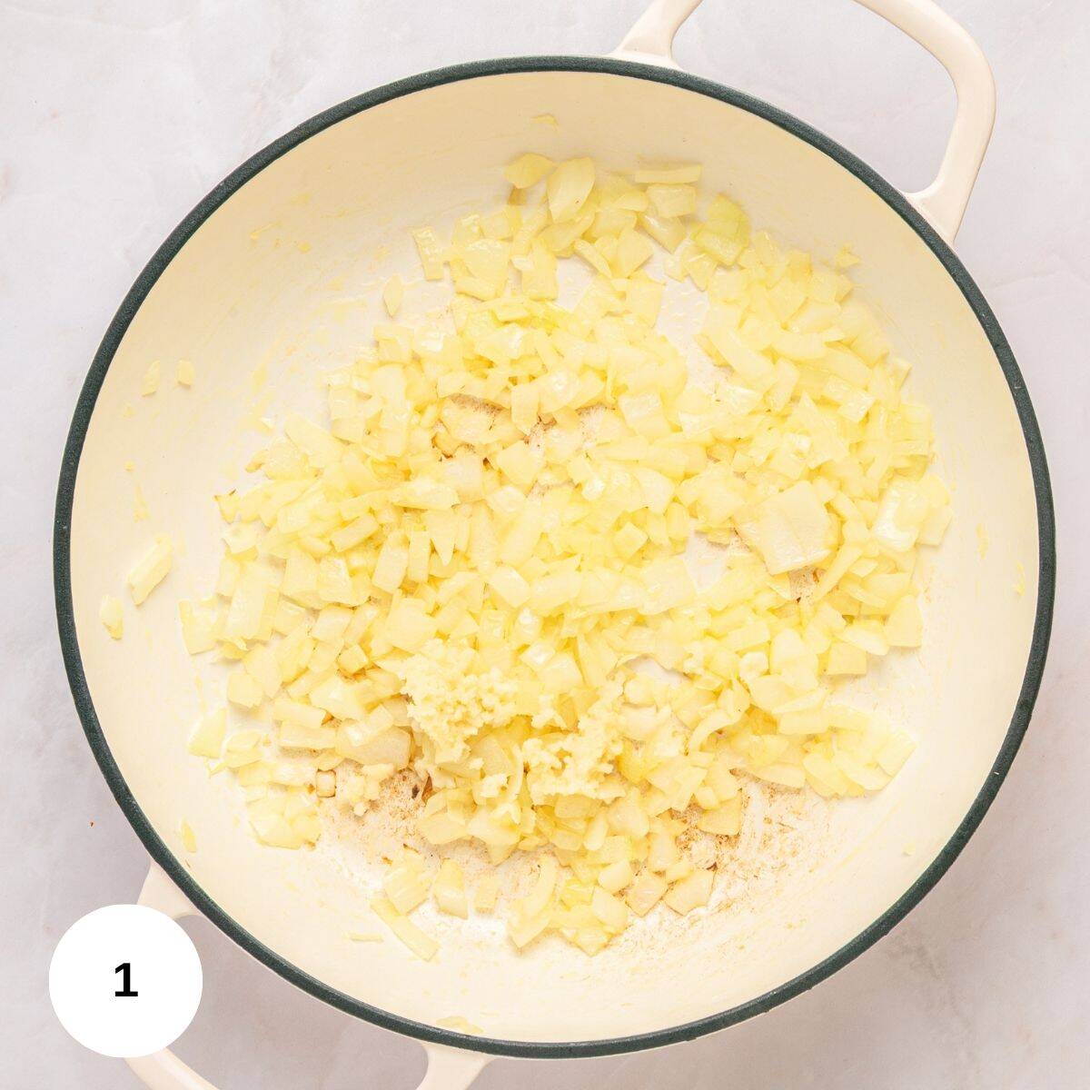 Chopped onions and minced garlic sautéing with turmeric in a large white pot, seen from above on a light surface. A round label with the number 1 appears in the lower left corner-perfect for starting Mediterranean Rice.
