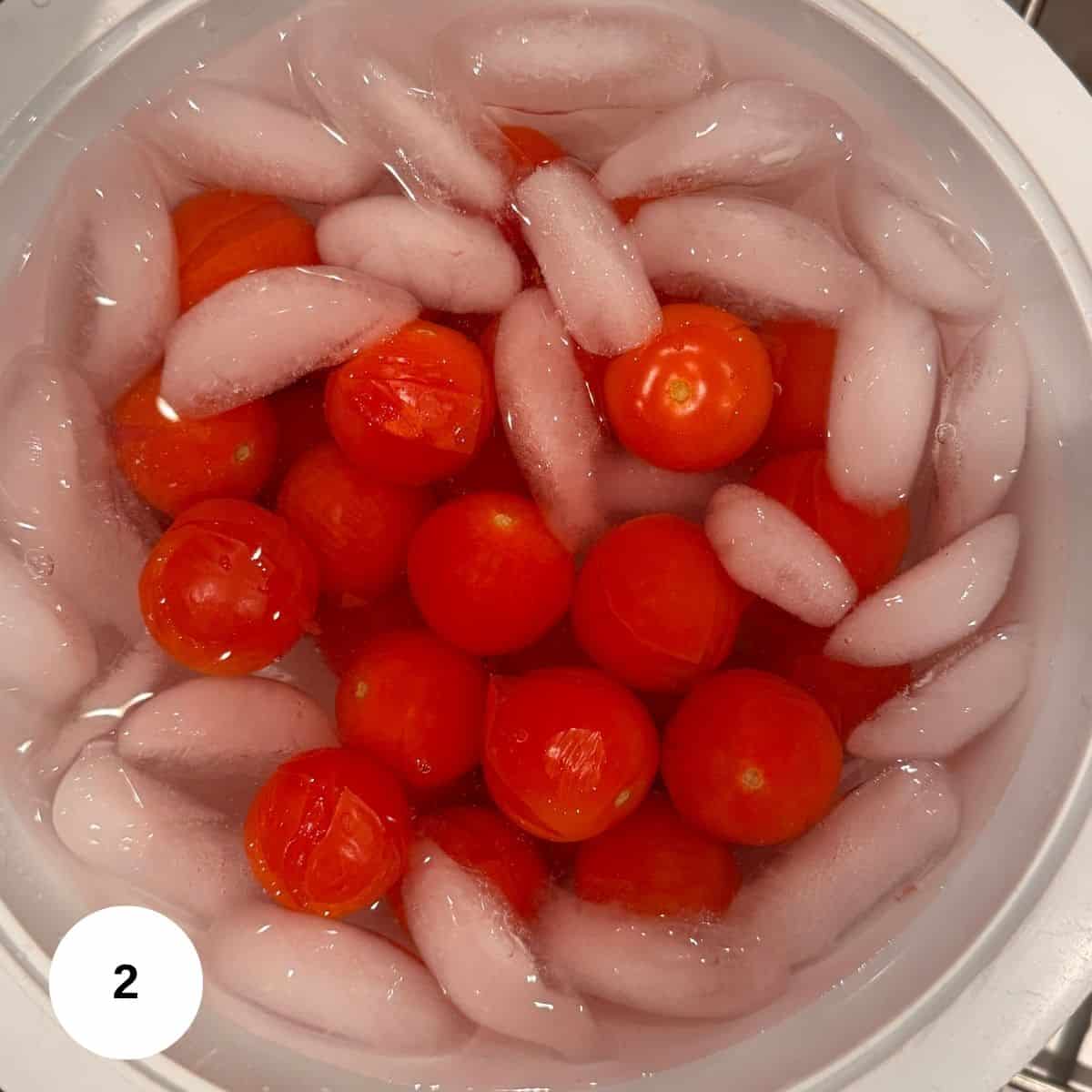 A bowl filled with cherry tomatoes submerged in ice water, surrounded by ice cubes, evokes a fresh Mediterranean vibe. A white circle with the number 2 is in the bottom left corner.