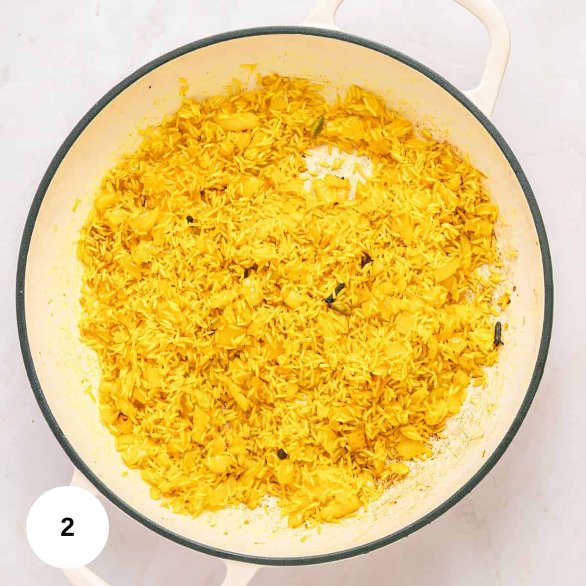 A white pot filled with fluffy Mediterranean rice, yellowed from turmeric and mixed with cabbage, sits on a light surface. Visible seasoning and cabbage pieces are scattered throughout. A 2 in a white circle is in the bottom left corner.