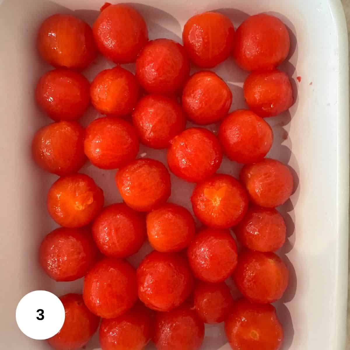 A white rectangular dish filled with neatly arranged, peeled cherry tomatoes in rows evokes a Mediterranean vibe. There is a white circle with the number 3 in the bottom left corner of the image.