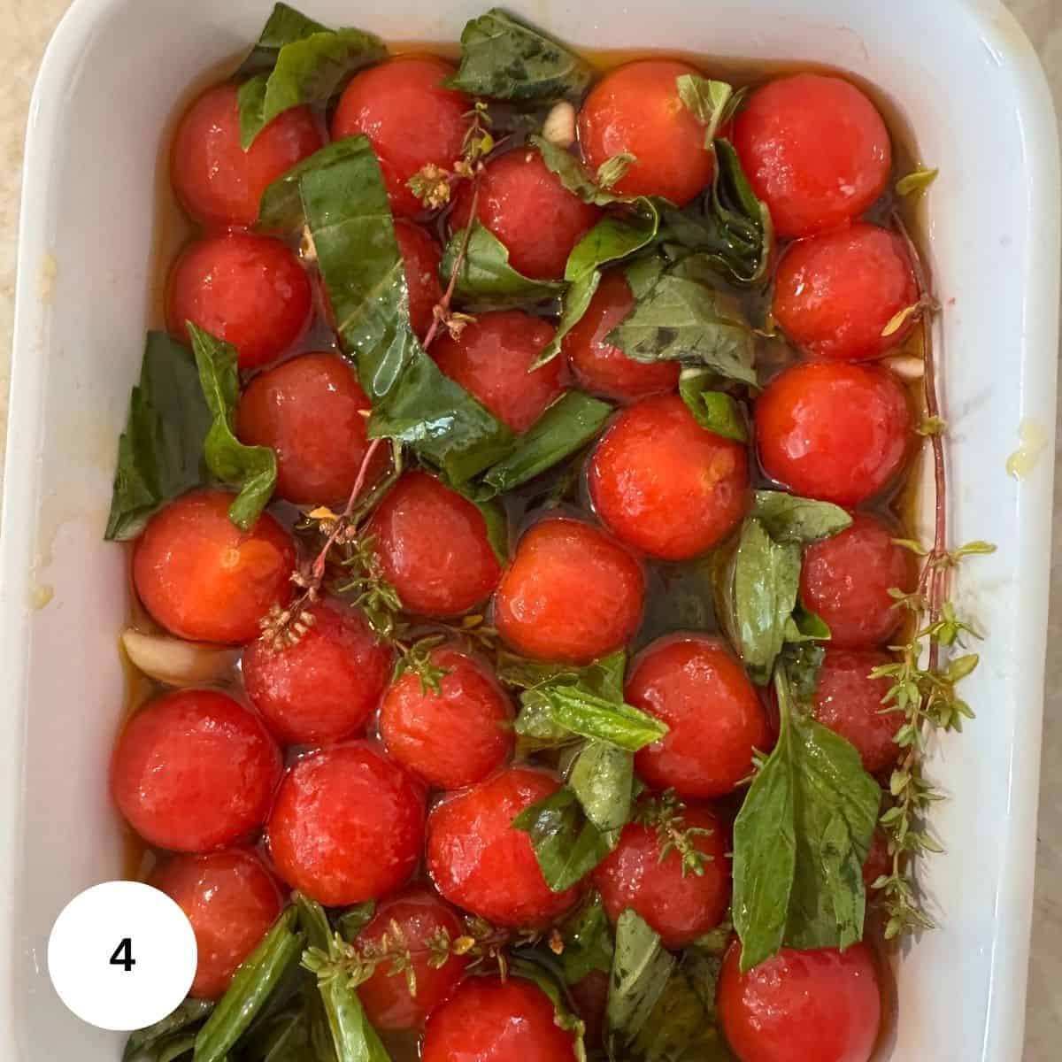 A white dish filled with round red cherry tomato confit, fresh green basil and thyme, and herbs, all marinated in a golden olive oil for a Mediterranean style touch. A white circle with the number 4 is in the bottom left corner.