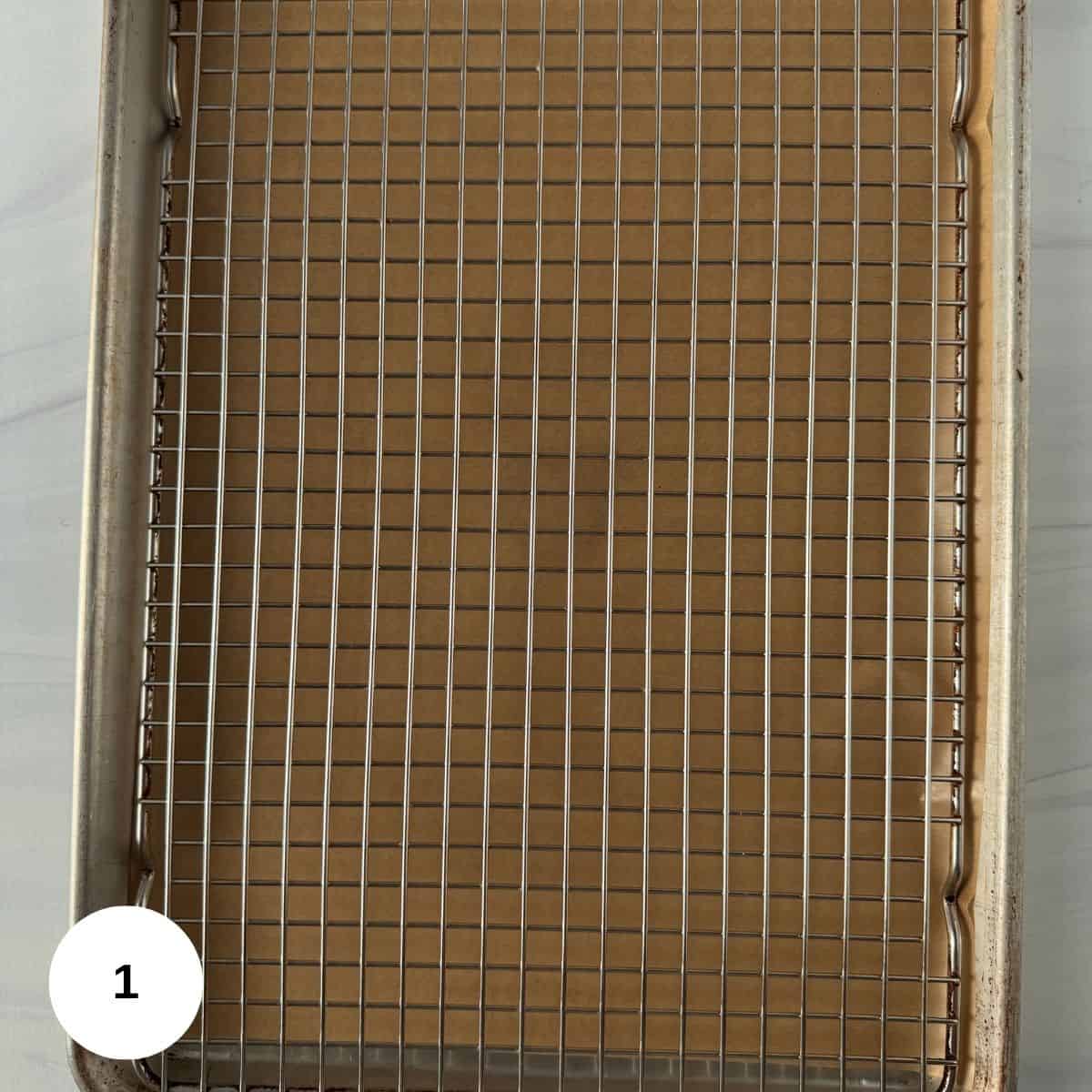 A baking sheet lined with parchment paper and topped with a metal cooling rack, perfect for preparing roasted zucchini slices. There is a white circle with the number 1 in the bottom left corner.