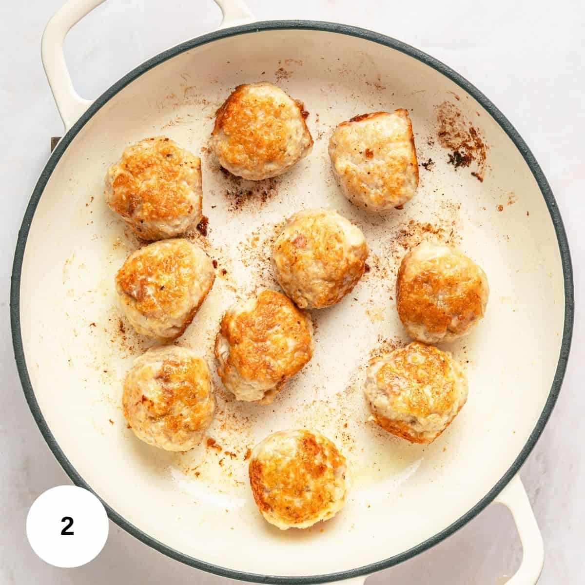 Ten browned Chicken Marsala Meatballs cook in a white skillet, surrounded by browned bits and oil. This one pan dish is pictured with a white circle labeled "2" in the lower left corner.