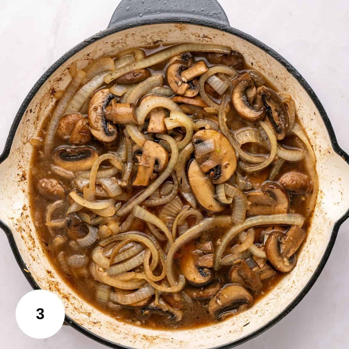 Sliced mushrooms and onions cooked in a brown sauce fill a white skillet with a black rim, creating a classic Chicken Marsala look on a light countertop-perfect for a one skillet, gluten free meal.